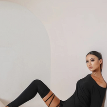 Load image into Gallery viewer, Woman in a black dress sitting down with her back against a wall