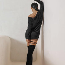 Load image into Gallery viewer, Woman in a black dress leaning against a wall with her back to the camera